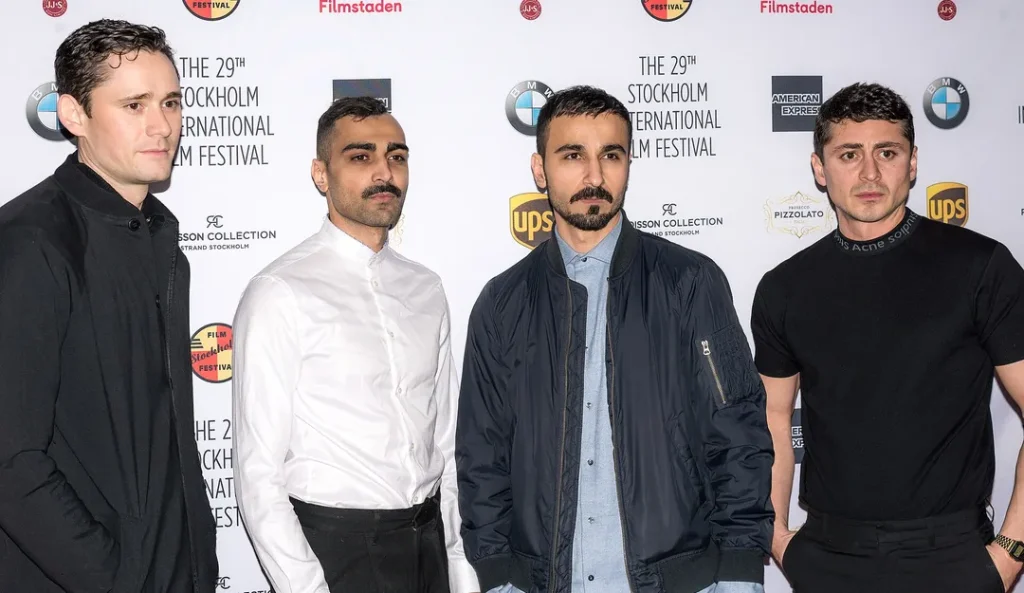 Fyra män på en red carpet-event vid Stockholms internationella filmfestival med sponsorlogotyper synliga i bakgrunden.